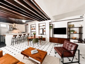 A modern living room with a wooden coffee table, a brown leather sofa, and a dining area with a kitchen in the background.