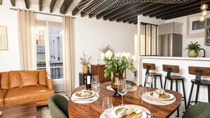 A modern dining area with a wooden table set for four, a sofa, and a kitchen in the background. - Spacious & modern property in Le Marais (Paris)