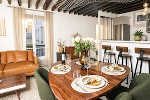 A modern dining area with a wooden table set for four, a sofa, and a kitchen in the background.