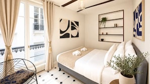 A bedroom with a bed, a chair, a plant, and artwork on the walls. - Spacious & modern property in Le Marais (Paris)