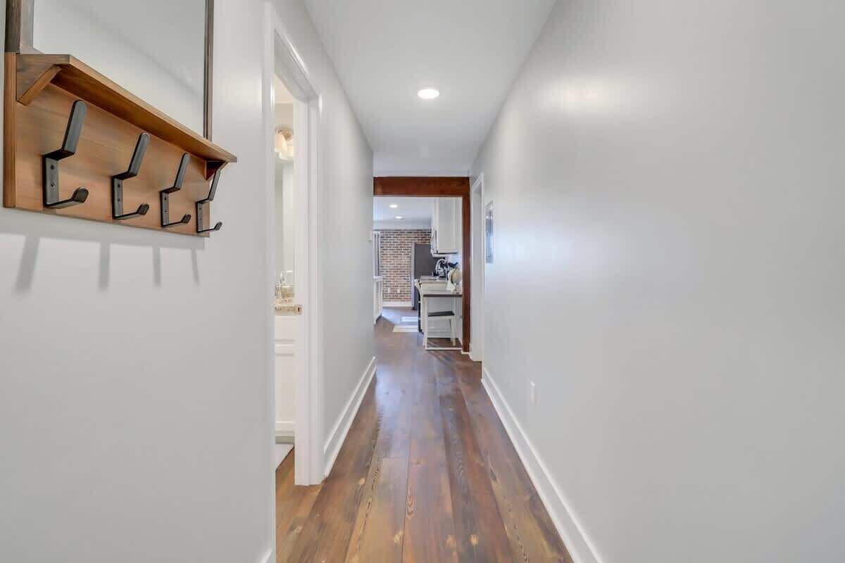 A hallway with wooden flooring, white walls, and a wooden shelf with hooks.