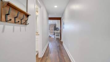A hallway with wooden flooring, white walls, and a wooden shelf with hooks.