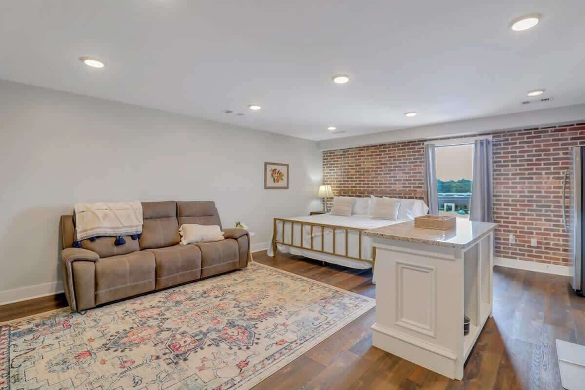 A spacious living room with a brown sofa, a white baby crib, and a patterned rug.