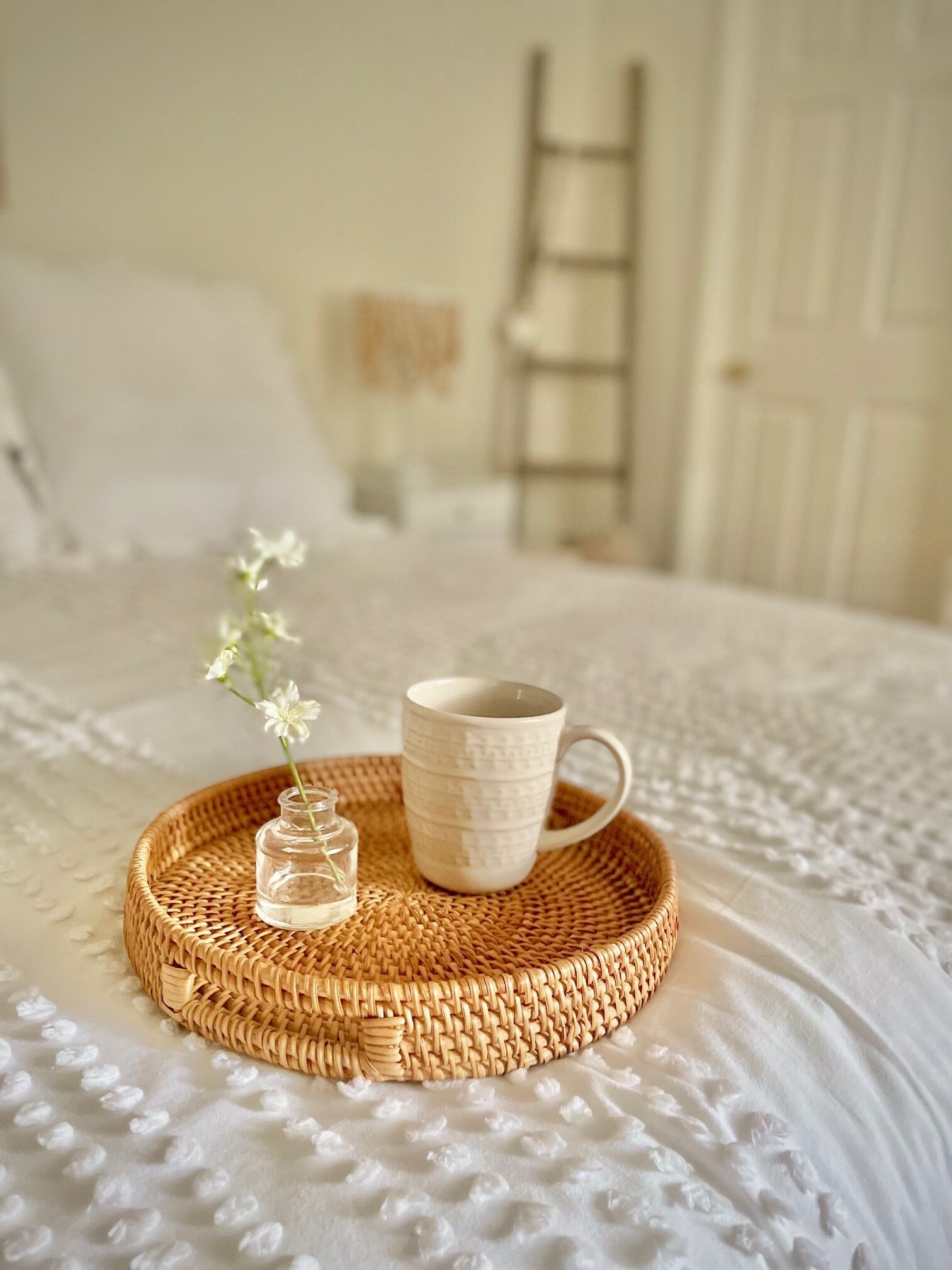 A wicker tray with a mug and a small vase on a textured bedspread.