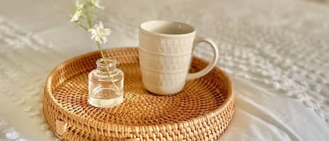 Una bandeja de mimbre con una taza y un pequeño florero sobre un edredón texturizado.