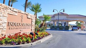 De ingang van de Indian Springs Golf and Country Club met een stenen bord, palmbomen en een heldere lucht.