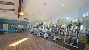 Een ruime fitnessruimte met cardioapparatuur, spiegels en een houten vloer.