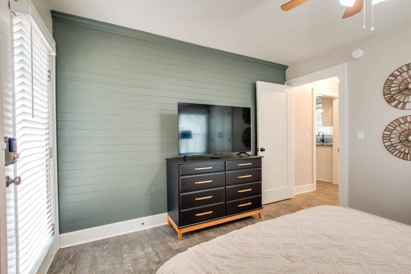 A bedroom with a bed, a dresser, a mirror, and a door leading to a bathroom.