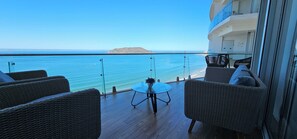 Un balcón con mobiliario de mimbre, una mesa de vidrio y vista al mar y una isla distante.