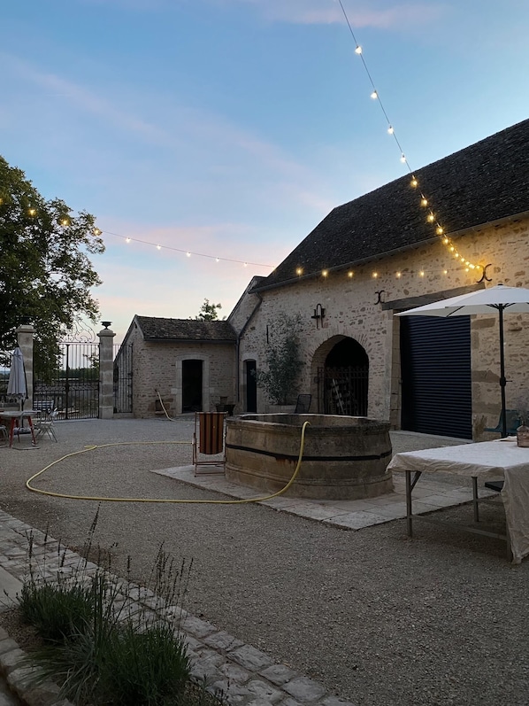 A rustic stone building with a gravel courtyard, outdoor seating, and string lights.