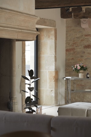 A room with a stone wall, a window, a plant, a table with a vase of flowers, and a bed.