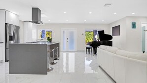 A modern kitchen with a central island, a dining area with a piano, and a white sofa.