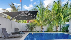 A swimming pool with lounge chairs and a covered area, surrounded by palm trees.