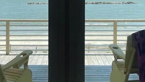 Udsigt fra et værelse med en træterrasse ud til en strand.