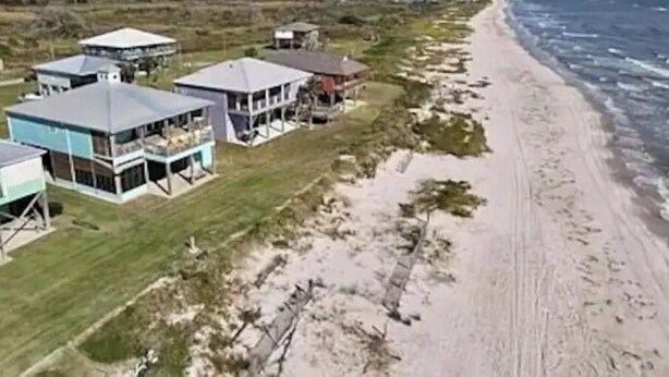 Oversigtsbillede af en kystejendom med flere huse, en sandstrand og havet.