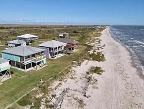 Vue aérienne d’une propriété située sur la côte, avec plusieurs maisons, une plage de sable et l’océan.