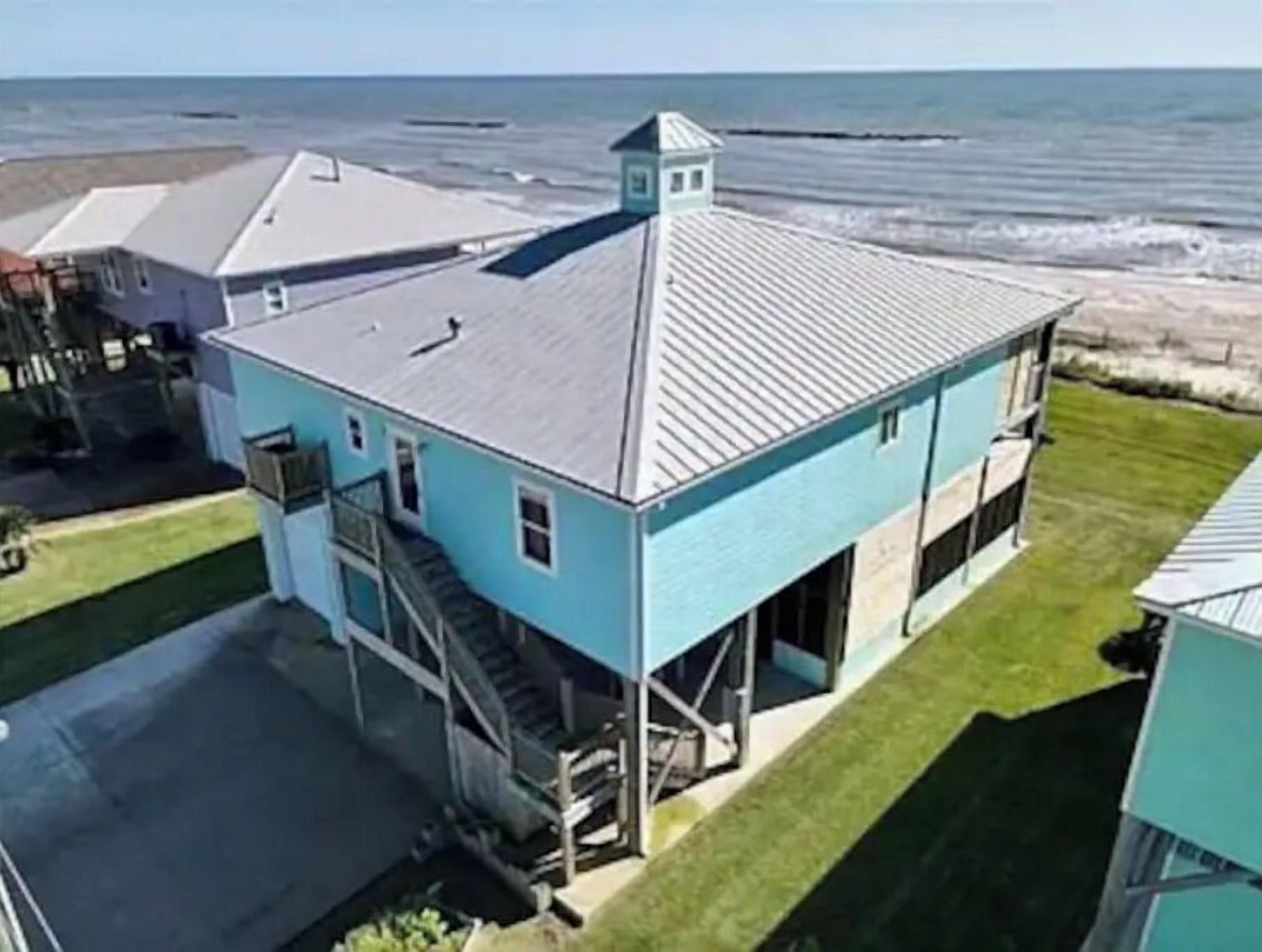 Een twee verdiepingen tellend huis met een blauwe gevel, een zichtbare trap en uitzicht op de oceaan.
