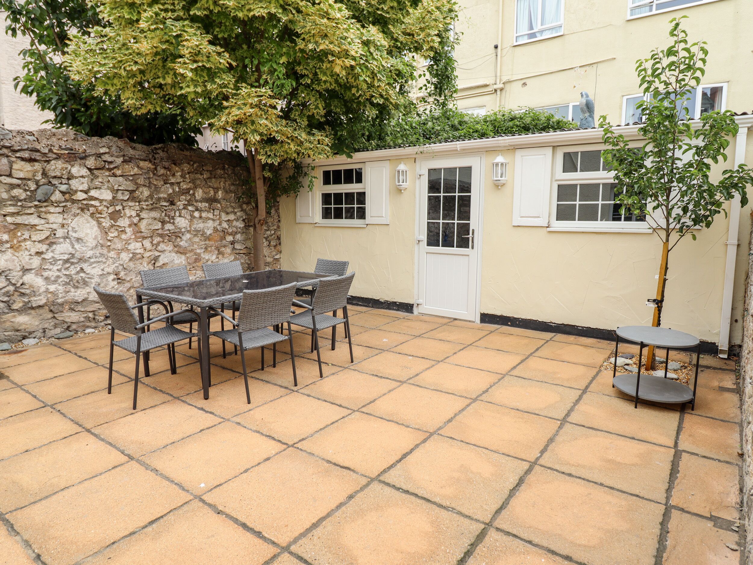 Eine Terrasse mit Tisch und Stühlen, eine Steinsäule und ein Gebäude mit Fenstern und einer Tür.