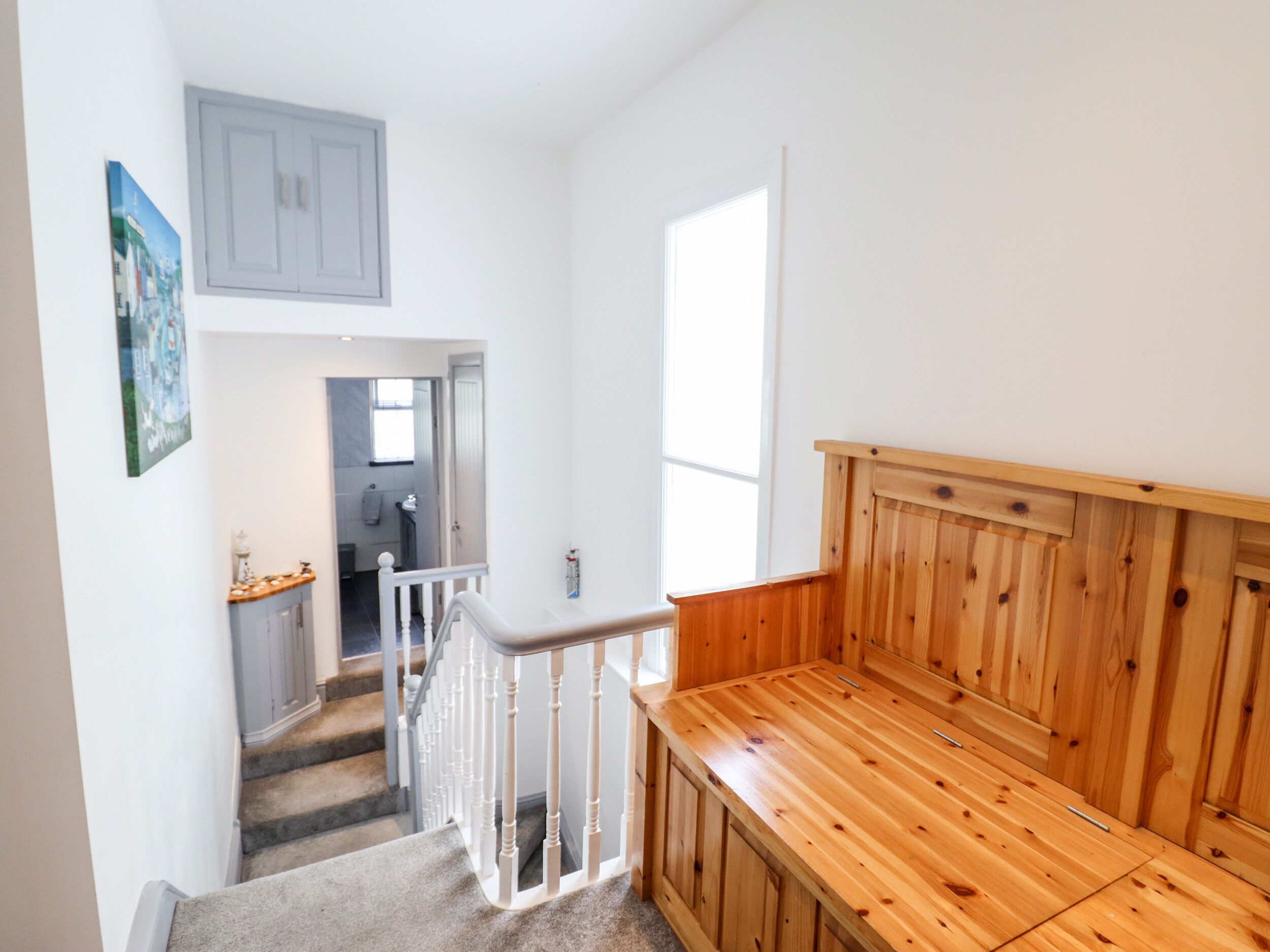 Un escalier menant à une chambre à coucher dotée d’une tête de lit en bois et d’une petite fenêtre.