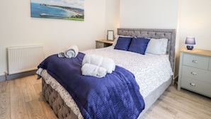 Un dormitorio con cama, mesita de noche, lámpara, un cuadro en la pared y un radiador.
