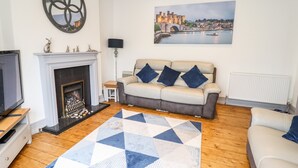Una sala de estar con chimenea, un sofá, un televisor y un cuadro de un castillo.