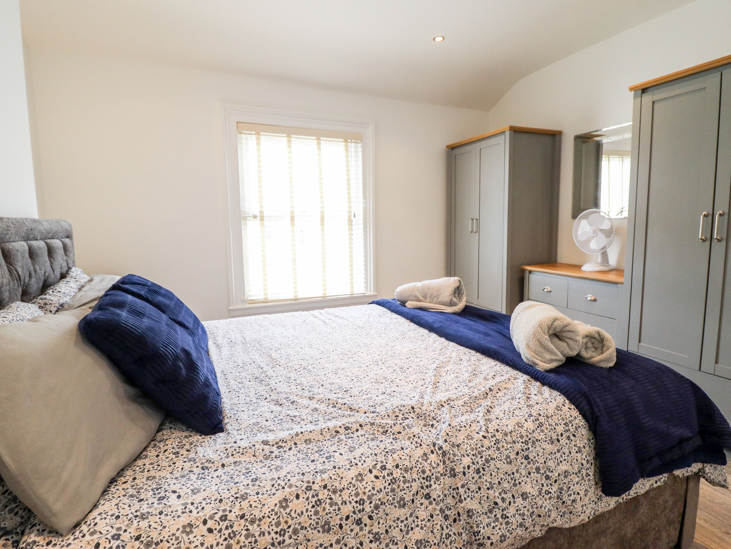 Een slaapkamer met een bed, een kledingkast, een raam en een ventilator.