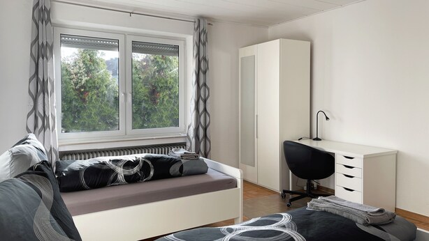 A modern bedroom with a bed, a desk, and a wardrobe.