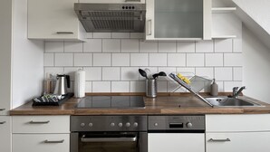 A modern kitchen with white cabinetry, a stainless steel range hood, a built-in oven, and a sink with a wooden countertop.