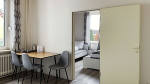 A modern room with a wooden ceiling, a dining table with chairs, a radiator, and a bed with a view of the outside.