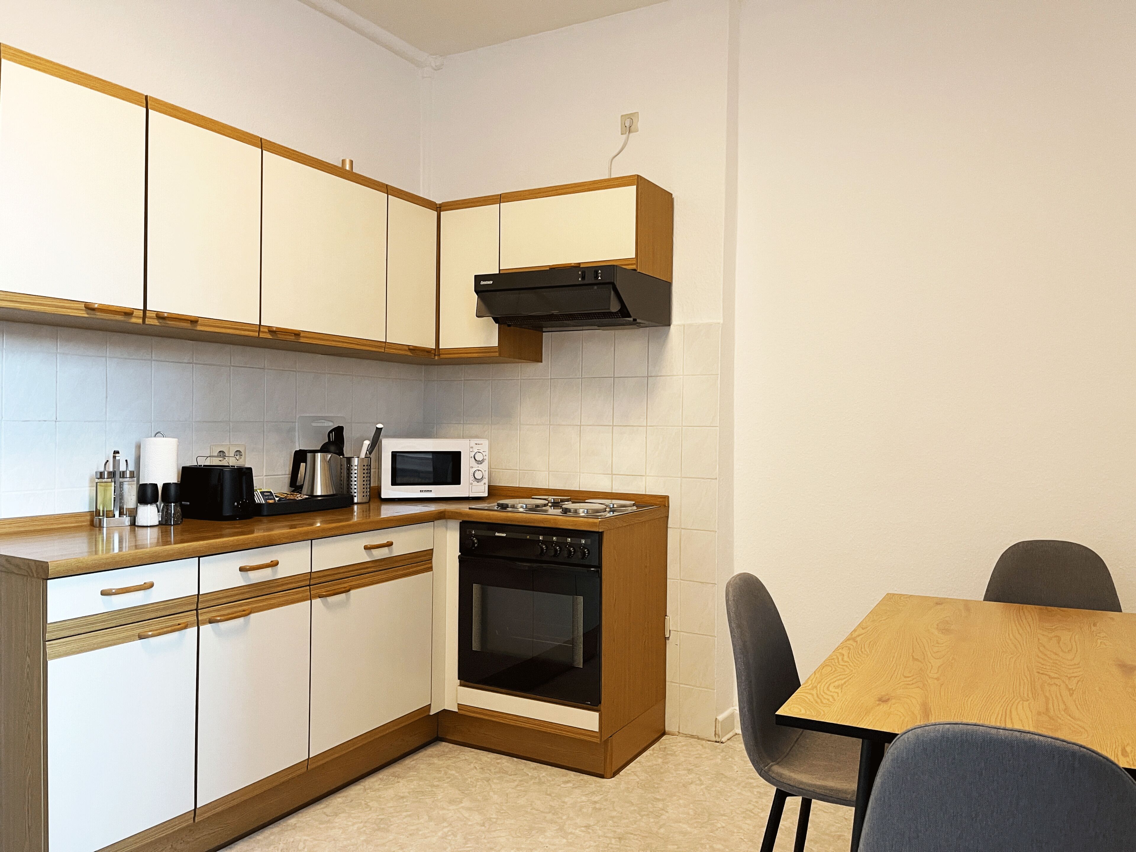 Una cocina compacta con gabinetes blancos, microondas, estufa y cafetera.