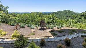 Ein angelegter Garten mit verschiedenen Sträuchern und Bäumen, einem Kiesweg und Blick auf einen bewaldeten Hügel im Hintergrund.
