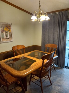 A dining room with a glass-top table surrounded by wooden chairs, a chandelier, and a painting on the wall.