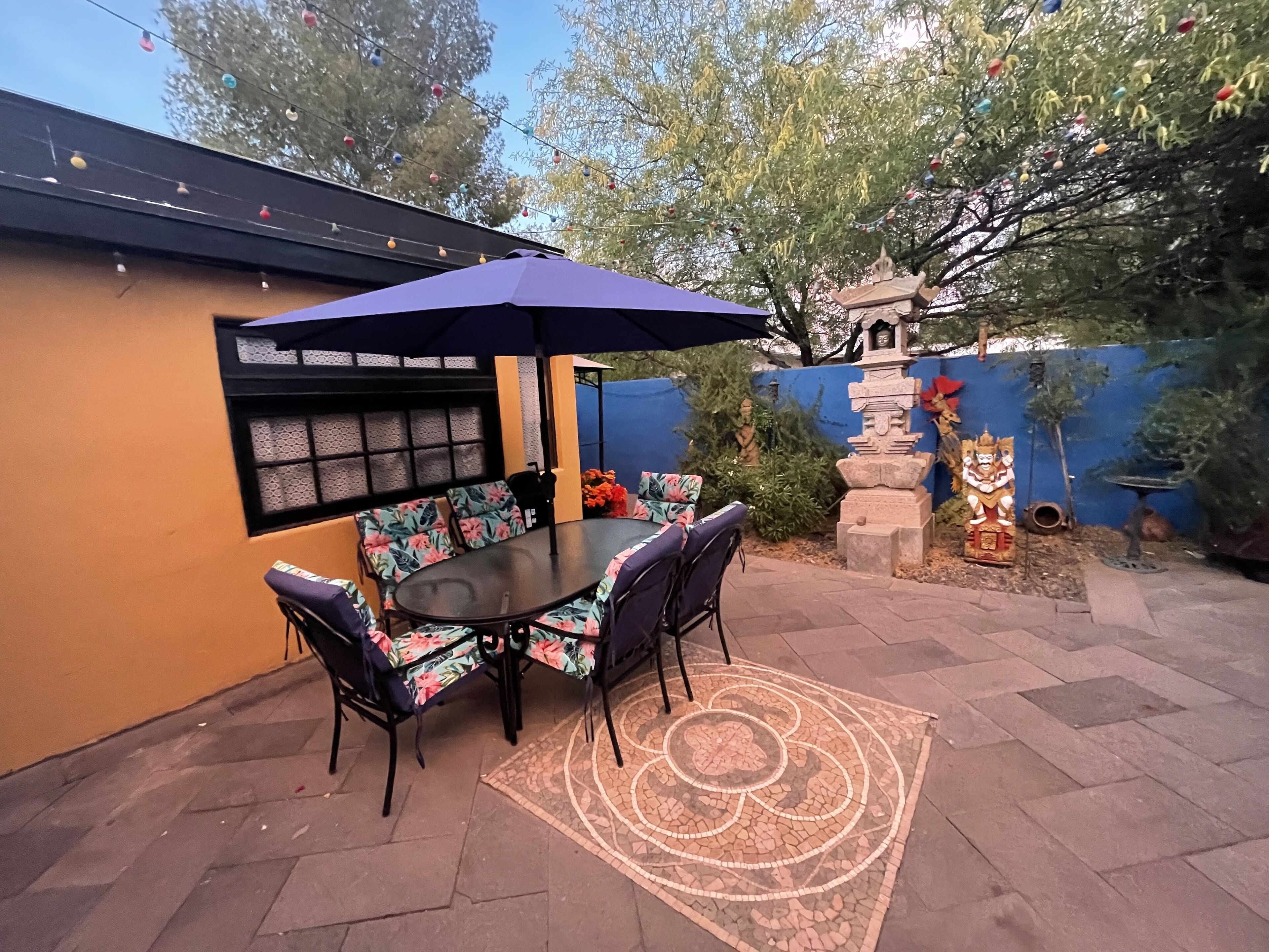 Une terrasse extérieure avec une table et des chaises, un tapis décoratif et une statue.