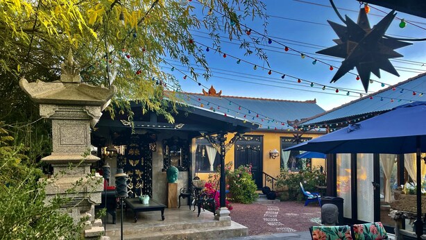 An outdoor patio area with stone seating, a decorative fountain, and string lights. - The Bali House Experience: Enjoy The Peace (Tucson)