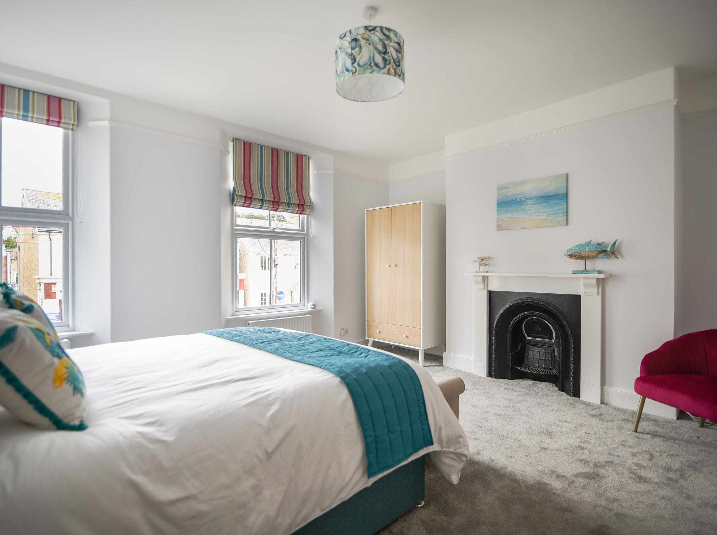Une chambre à coucher avec un lit, une fenêtre ornée de rideaux à rayures, une armoire, une cheminée et un fauteuil rouge.