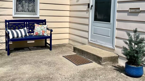 A house with a blue bench outside, a white door, and a small potted plant.