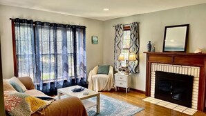A living room with a sofa, a coffee table, a fireplace, and a window with curtains.