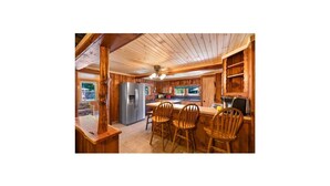 A wooden cabin interior with a kitchen area featuring a refrigerator, wooden chairs, and a dining table. - Charming cottage overlooking pond and meadows (Holtwood)