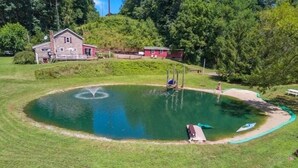 A circular pond with a fountain, surrounded by a grassy area and a small building. - Charming cottage overlooking pond and meadows (Holtwood)