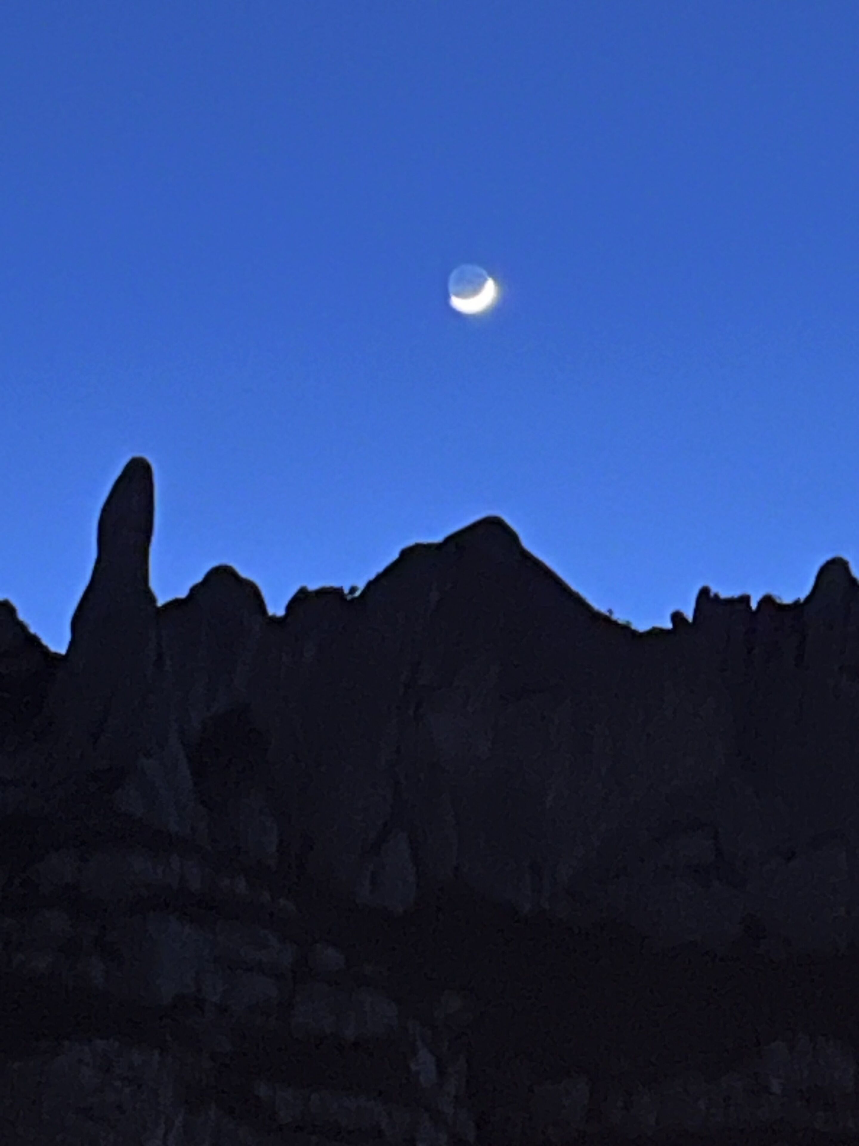 Silueta de una cordillera contra un cielo nocturno con luna visible.
