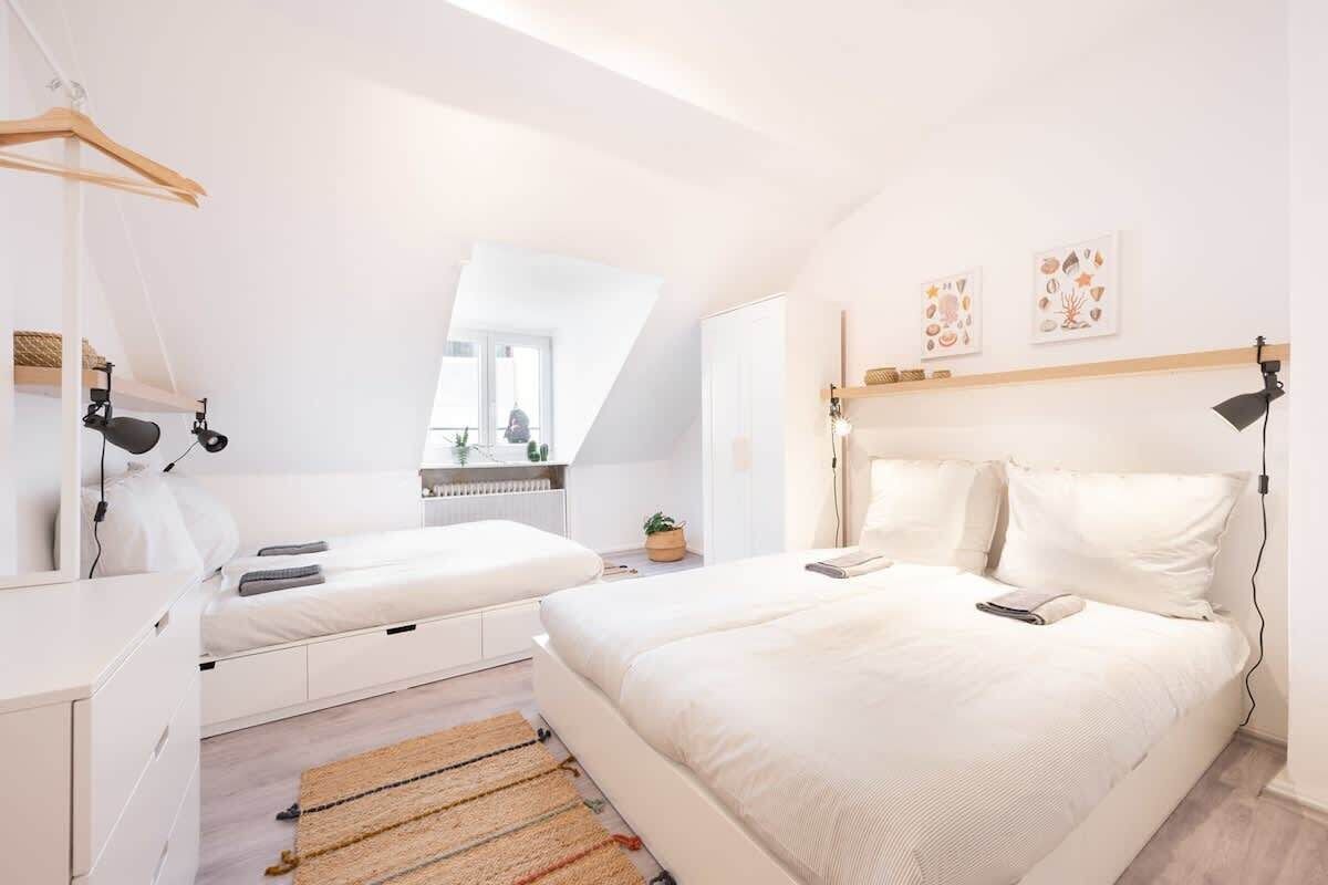 Ein modernes Schlafzimmer mit einem großen Bett, einem kleineren Bett, einem Schreibtisch und einem Spiegel.