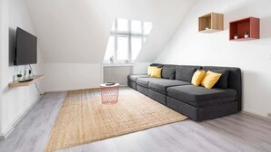 Una sala de estar moderna con un sofá seccional gris, un televisor de pantalla plana y un ventanal grande.