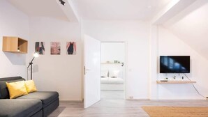 Una sala de estar moderna con un sofá gris, un televisor de pantalla plana montado en la pared y una puerta que da a otra habitación.