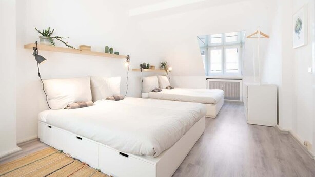 Un dormitorio moderno con dos camas, un radiador, una lámpara colgante y una ventana con vistas.
