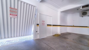 Un estacionamiento limpio y vacío con una puerta blanca, una franja amarilla y negra en el suelo y un letrero que indica acceso para peatones.