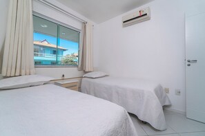 Ein Hotelzimmer mit zwei Betten, einem Fenster mit Vorhängen, einer Klimaanlage und einer Tür.