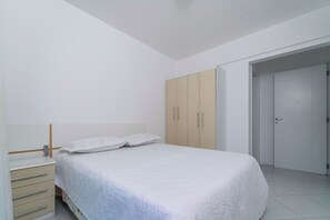 A bedroom with a bed, a wardrobe, a bedside table, and a door. - 839 -Apartamento 2 dormitórios Bombinhas (Bombinhas)