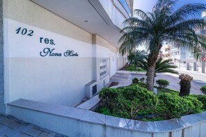 A building with a sign reading "102 res. Nona Marta" and a small garden area with a palm tree and shrubs. - 839 -Apartamento 2 dormitórios Bombinhas (Bombinhas)
