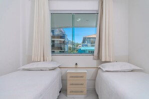 A bedroom with two single beds, a small bedside table, and a window with curtains.