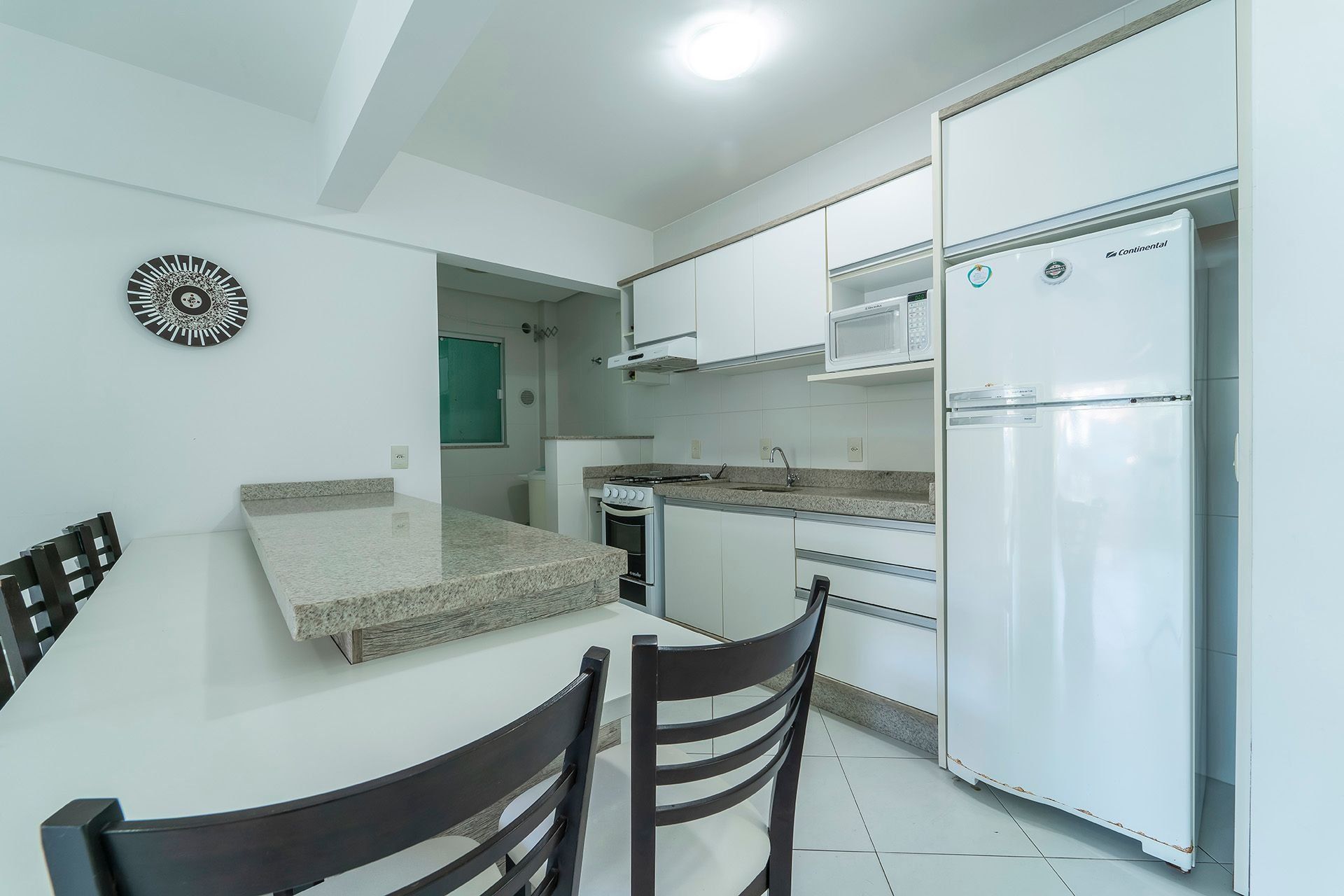 A compact kitchen with white cabinets, a built-in microwave, a stainless steel refrigerator, and a dining area with a table and chairs.